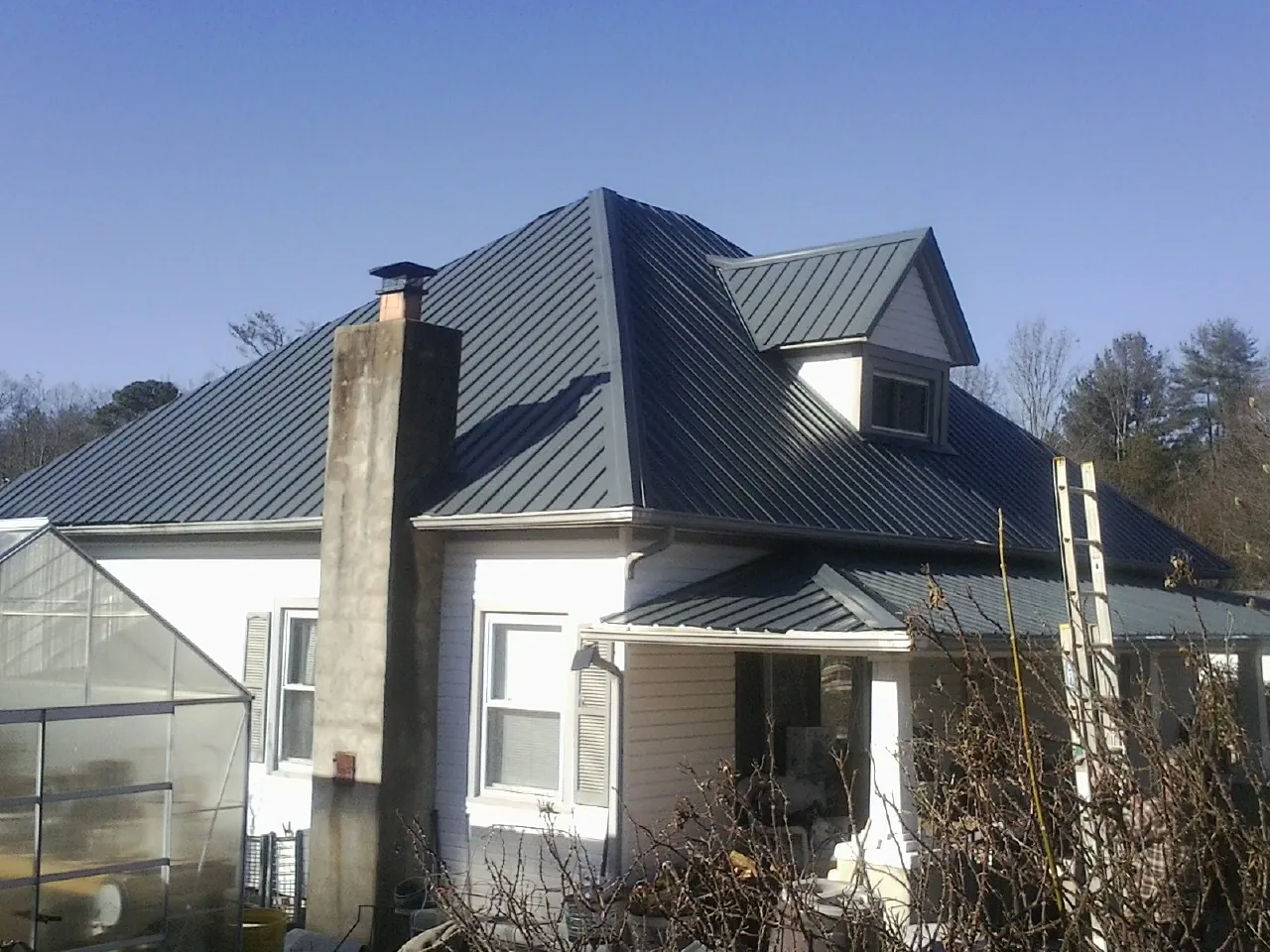 Dark blue standing seam metal roof on a white farmhouse with dormer — Slate & Tile Roof Repair by Roofing Brothers in Clemons