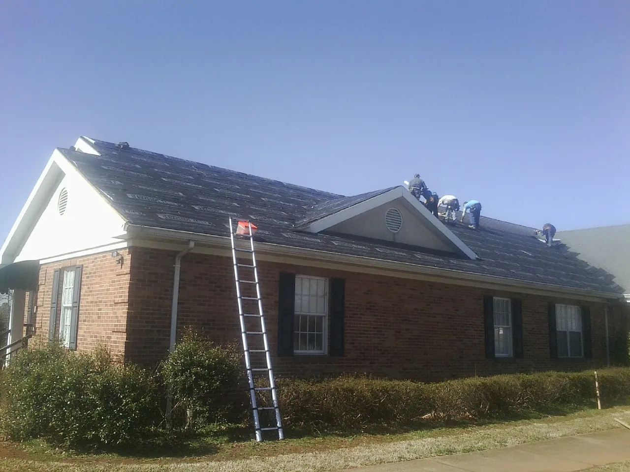 Crew tearing shingles off a brick ranch roof with a ladder set — Emergency Roof Repair work by our crew in Clemons