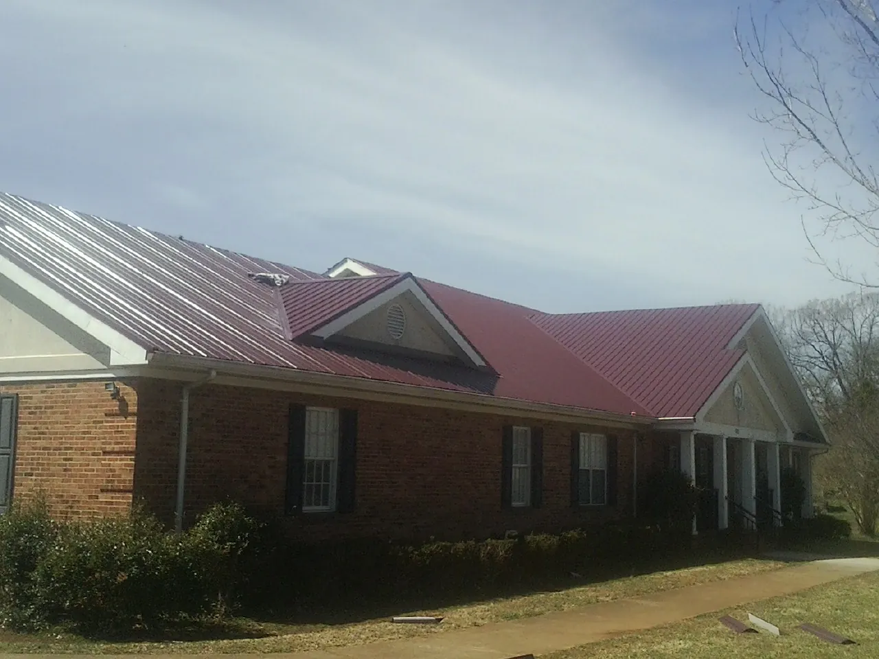 Red metal roof with gabled entries on a long brick building, from a Hail Damage Roof Repair job in Clemons