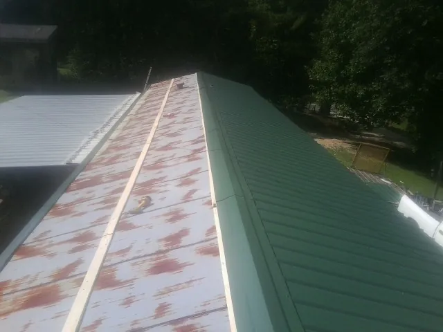 Old rusted panels beside newly installed green metal roofing — Wind Damage Roof Repair by Roofing Brothers in Clemons