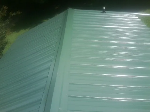New green metal panels meeting at the ridge of a roof — Flat Roof Repair work by our crew in Clemons