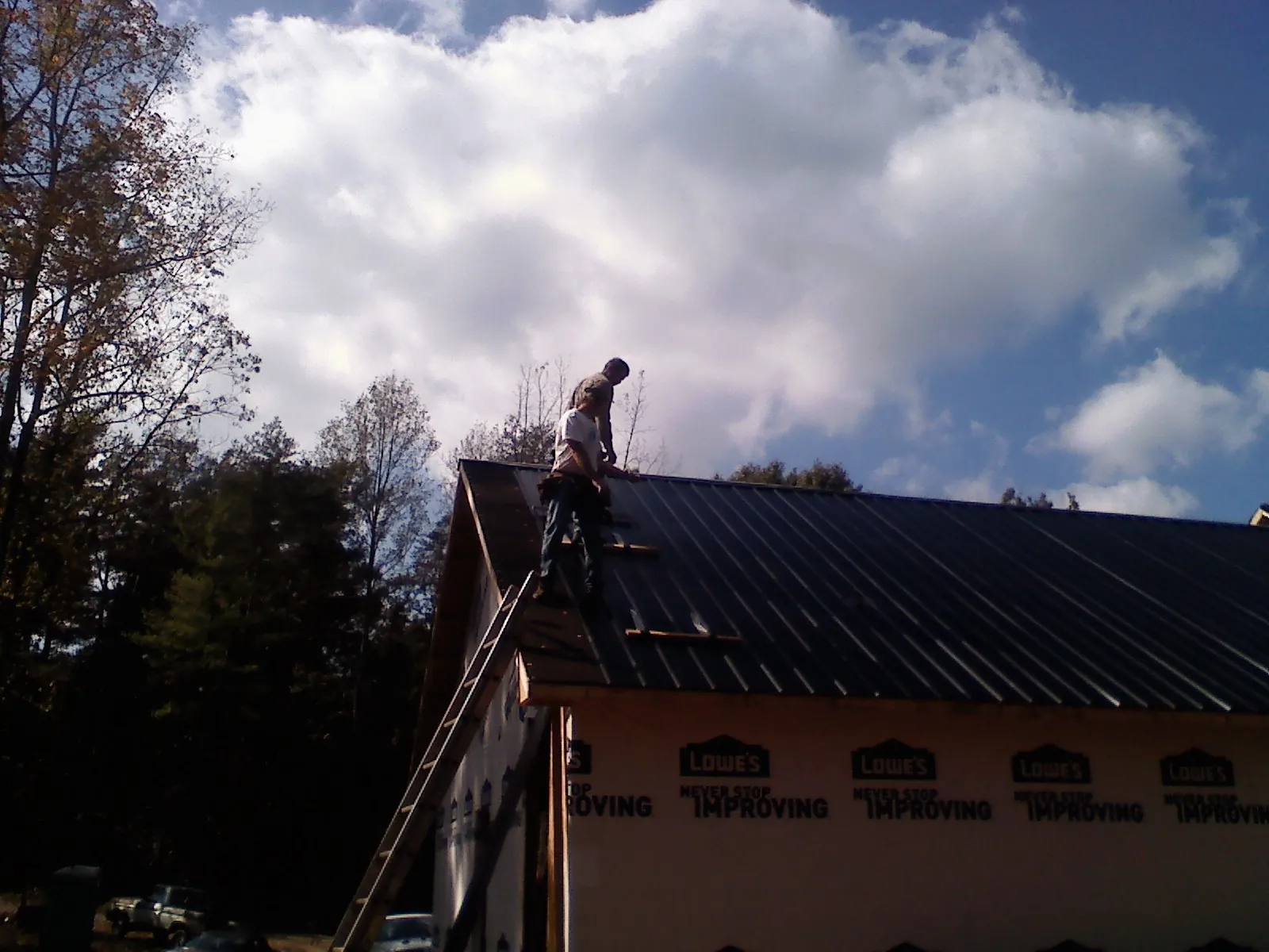 Roofer fastening dark metal panels high against a cloudy sky, from a Roof Inspection job in Clemons