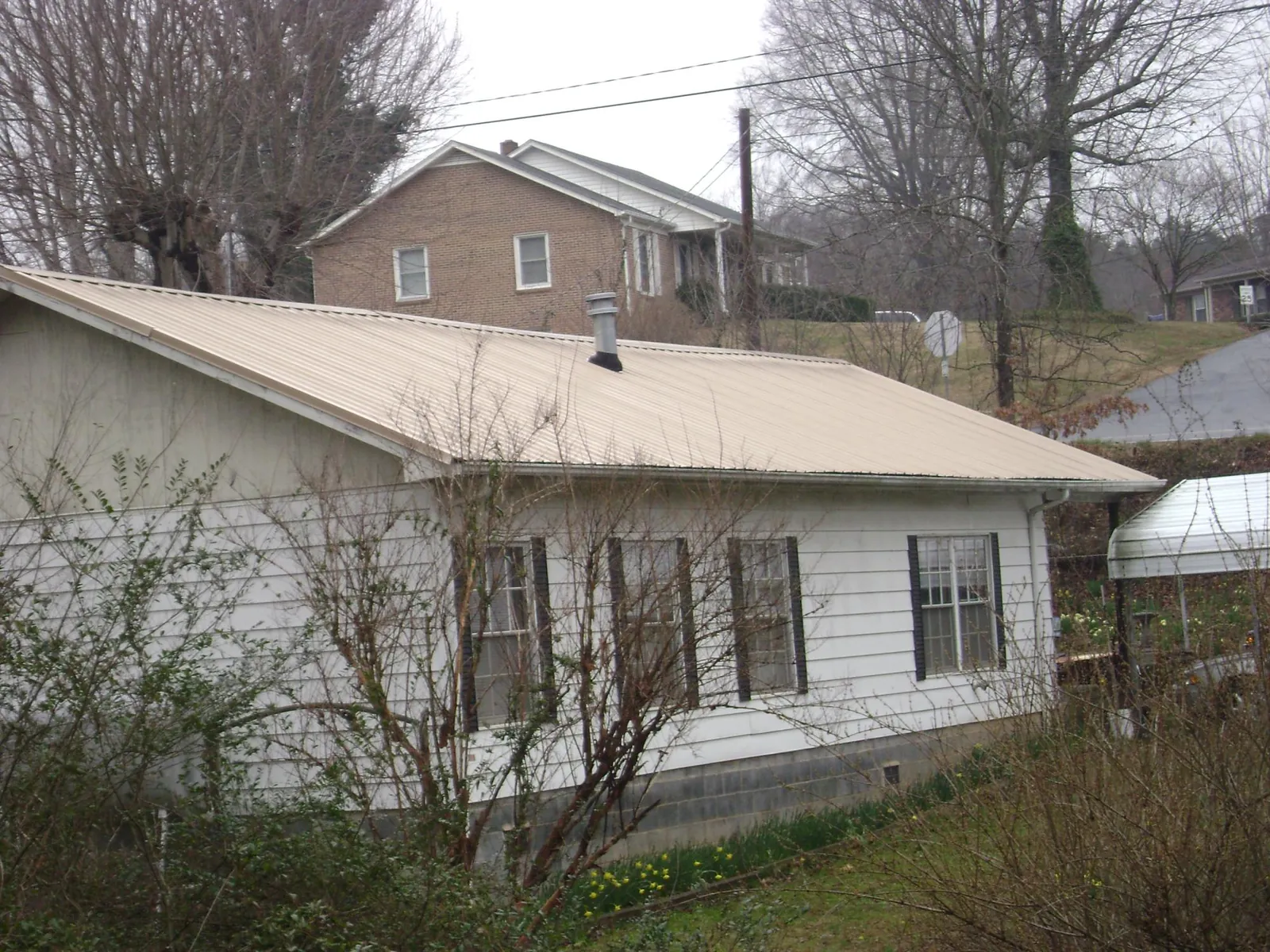 Tan metal roof on a white sided house set into a hillside — Commercial Roofing by Roofing Brothers in Clemons