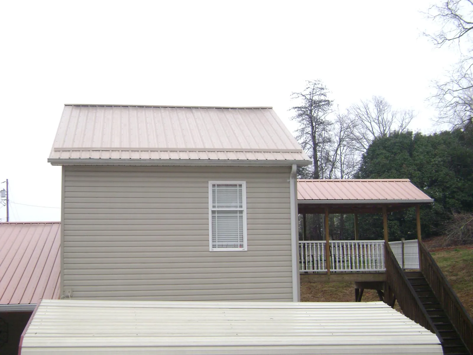 Tan metal roofs on a two story addition and attached porch, from a Roof Replacement job in Clemons